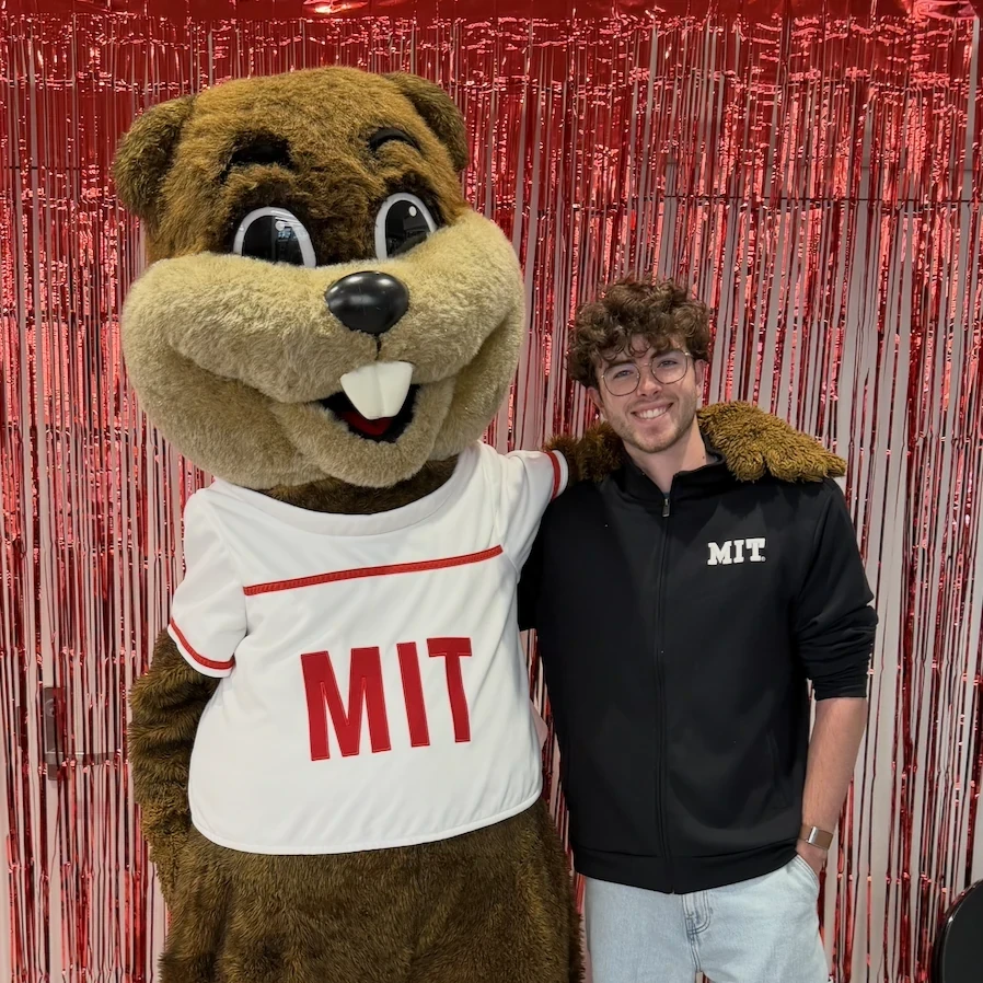 Alexandre in an MIT jacket beside Tim the Beaver, MIT’s mascot, in its MIT jersey.
